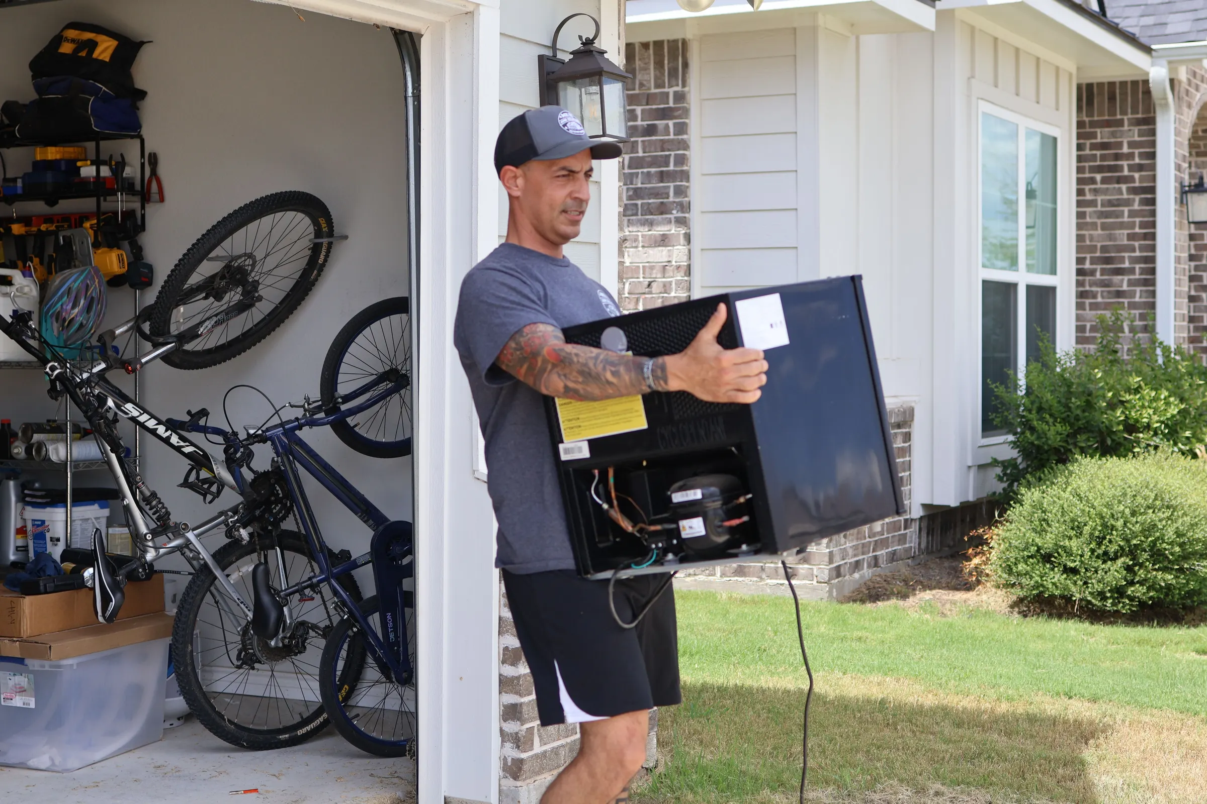 Eddie carrying a small black refrigerator out of a garage